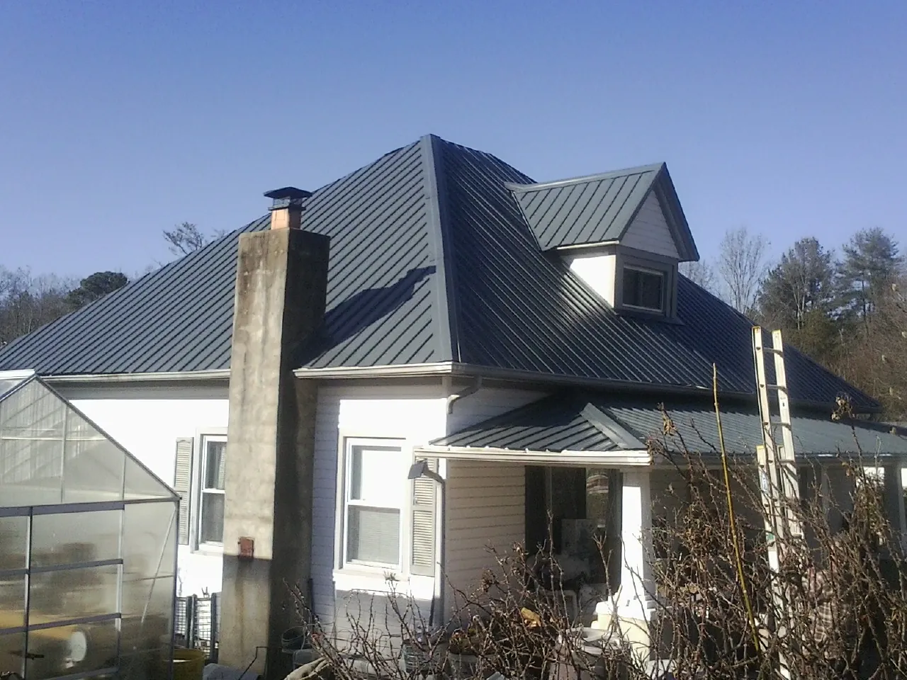 Dark blue standing seam metal roof on a white farmhouse with dormer — Slate & Tile Roof Repair by Roofing Brothers in Central Islip