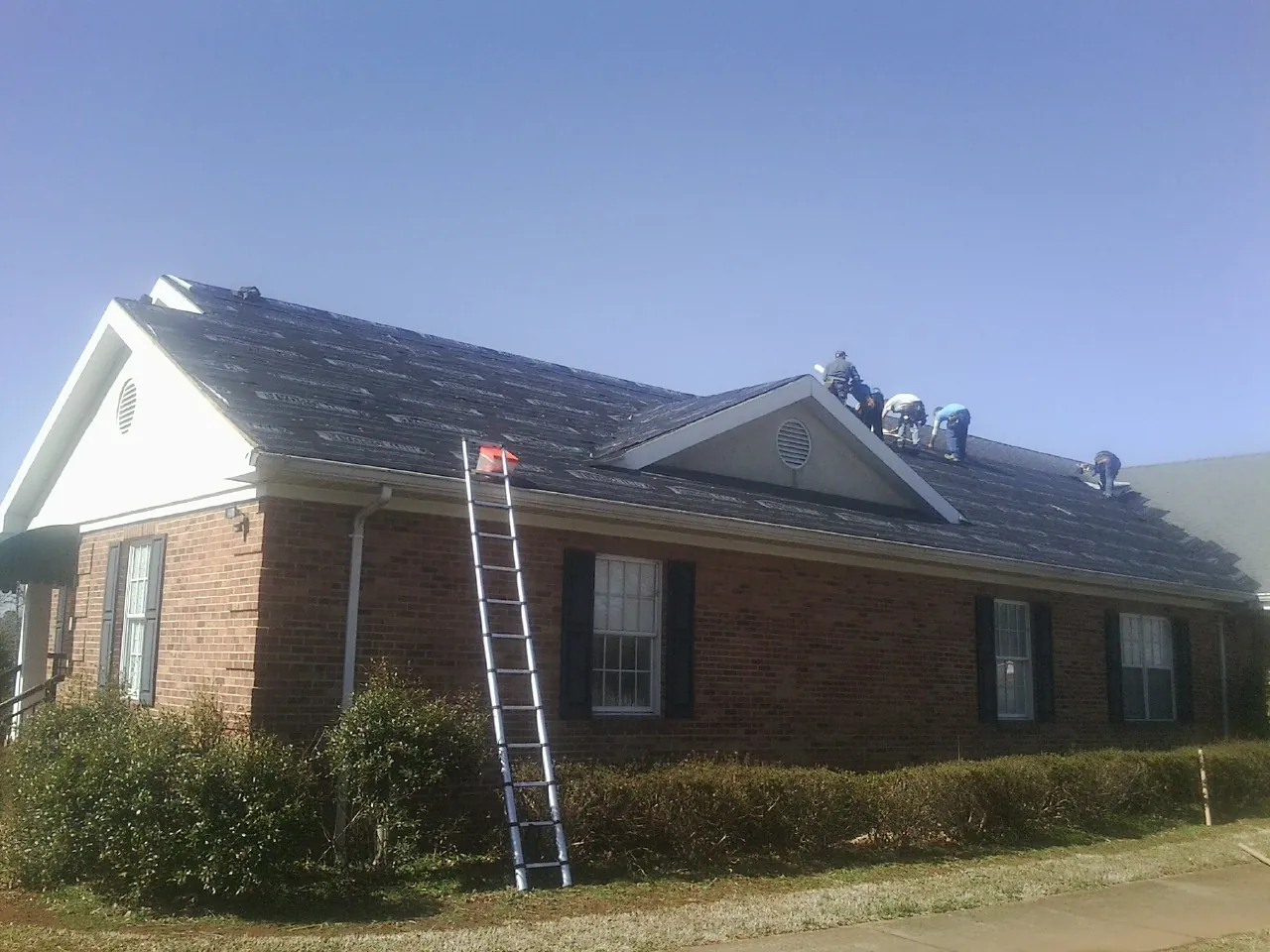 Crew tearing shingles off a brick ranch roof with a ladder set — Emergency Roof Repair work by our crew in Central Islip
