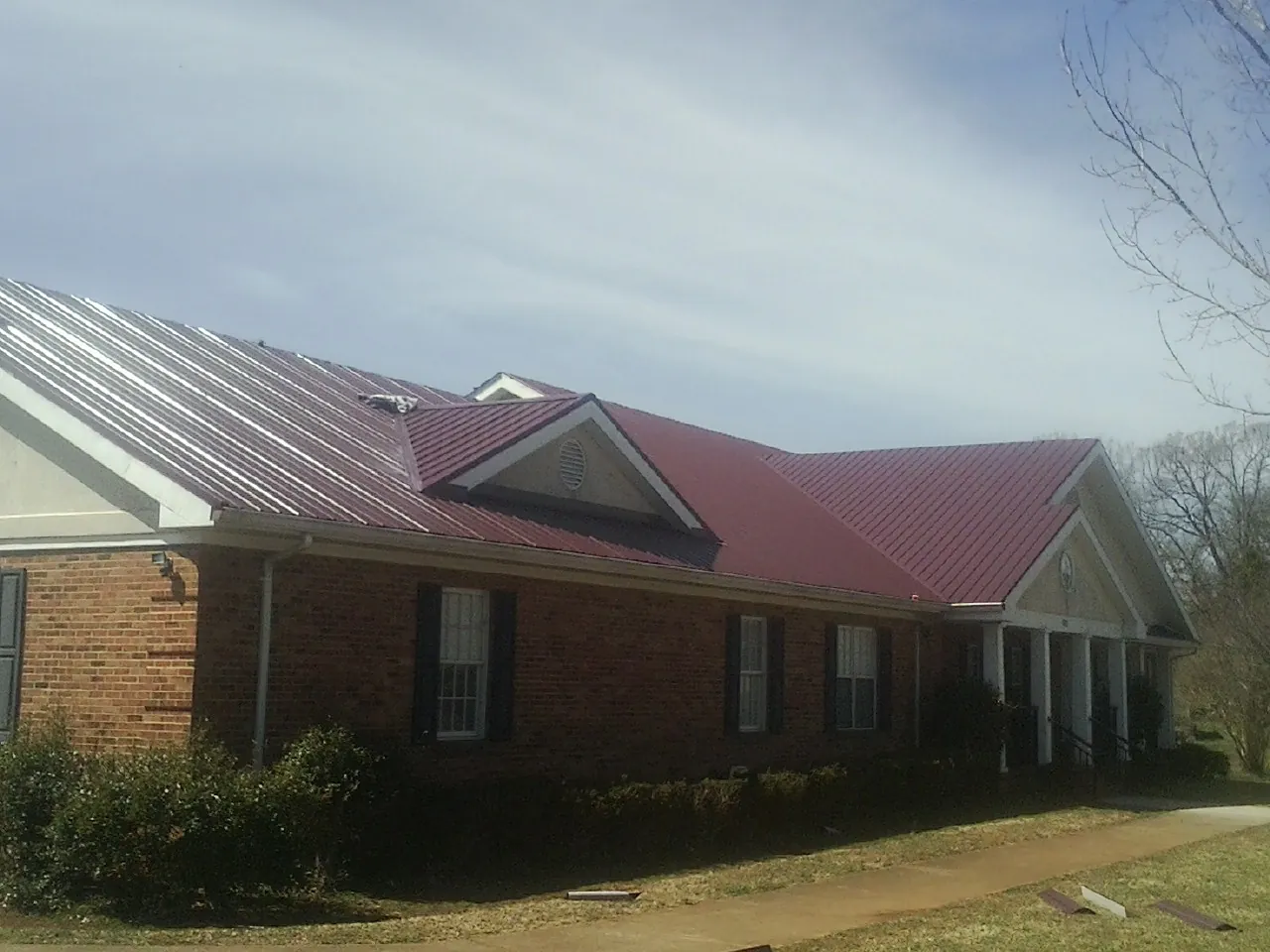 Red metal roof with gabled entries on a long brick building, from a Hail Damage Roof Repair job in Central Islip