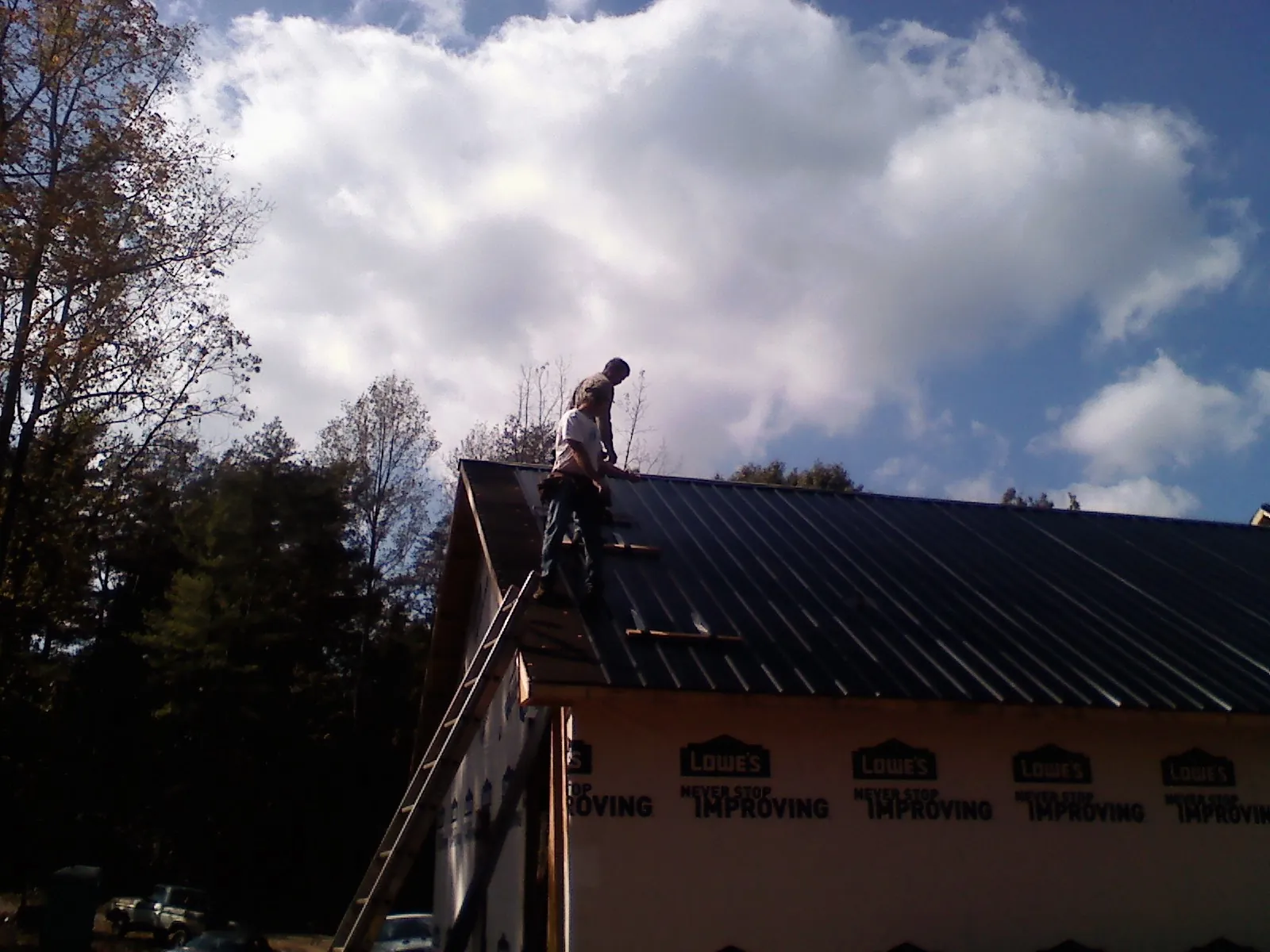 Roofer fastening dark metal panels high against a cloudy sky, from a Roof Inspection job in Central Islip