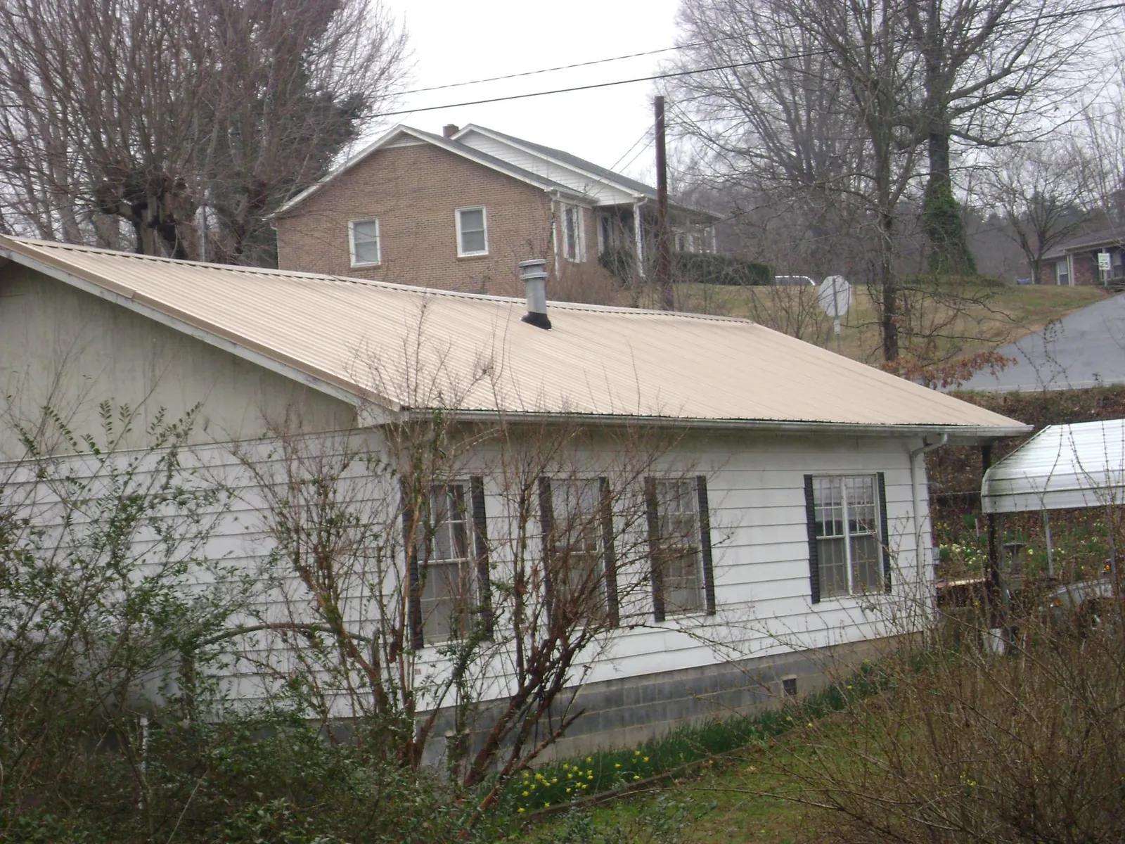 Tan metal roof on a white sided house set into a hillside — Commercial Roofing by Roofing Brothers in Central Islip